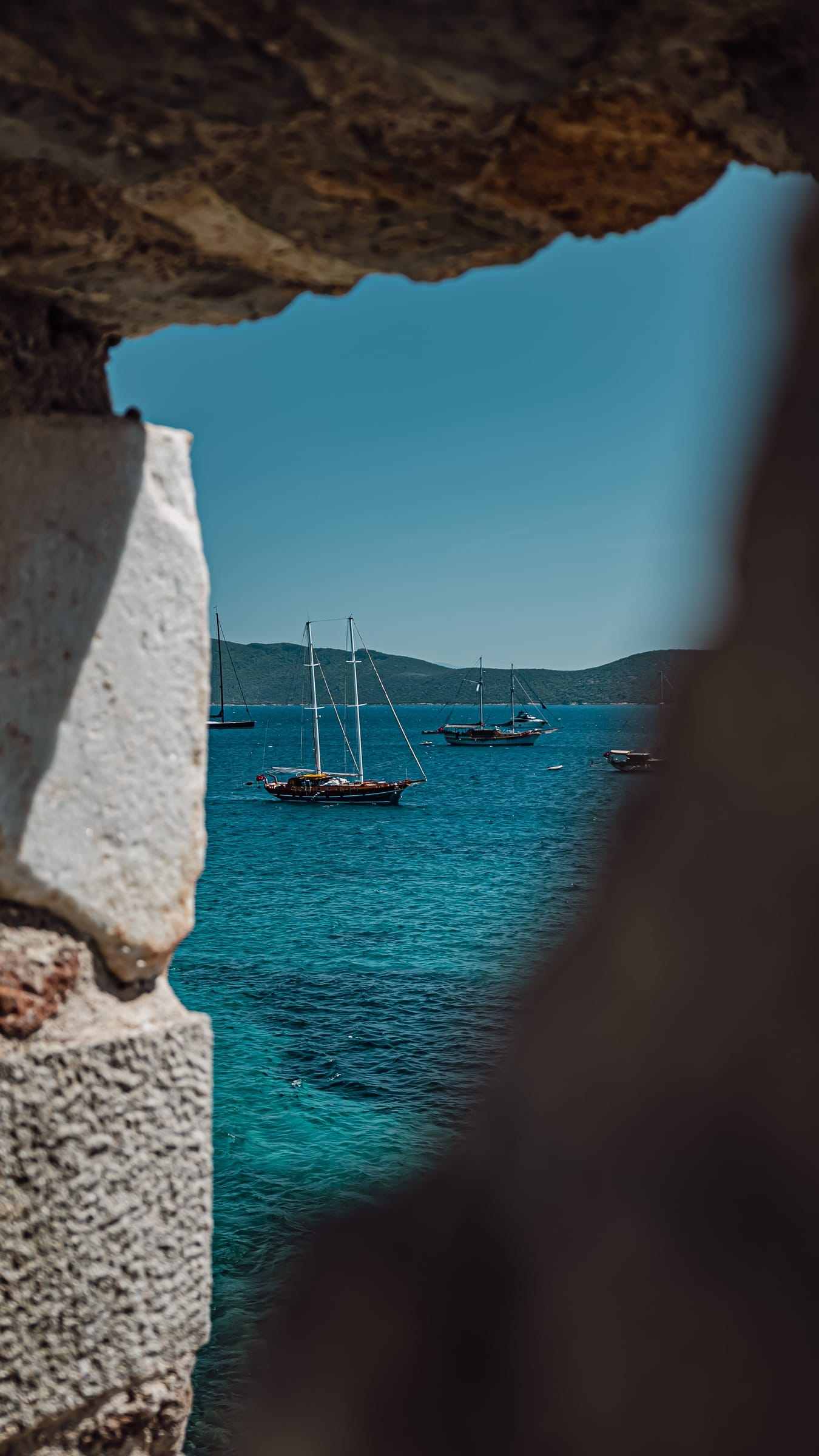 Gulets and sea seen through a gap in a stone wall