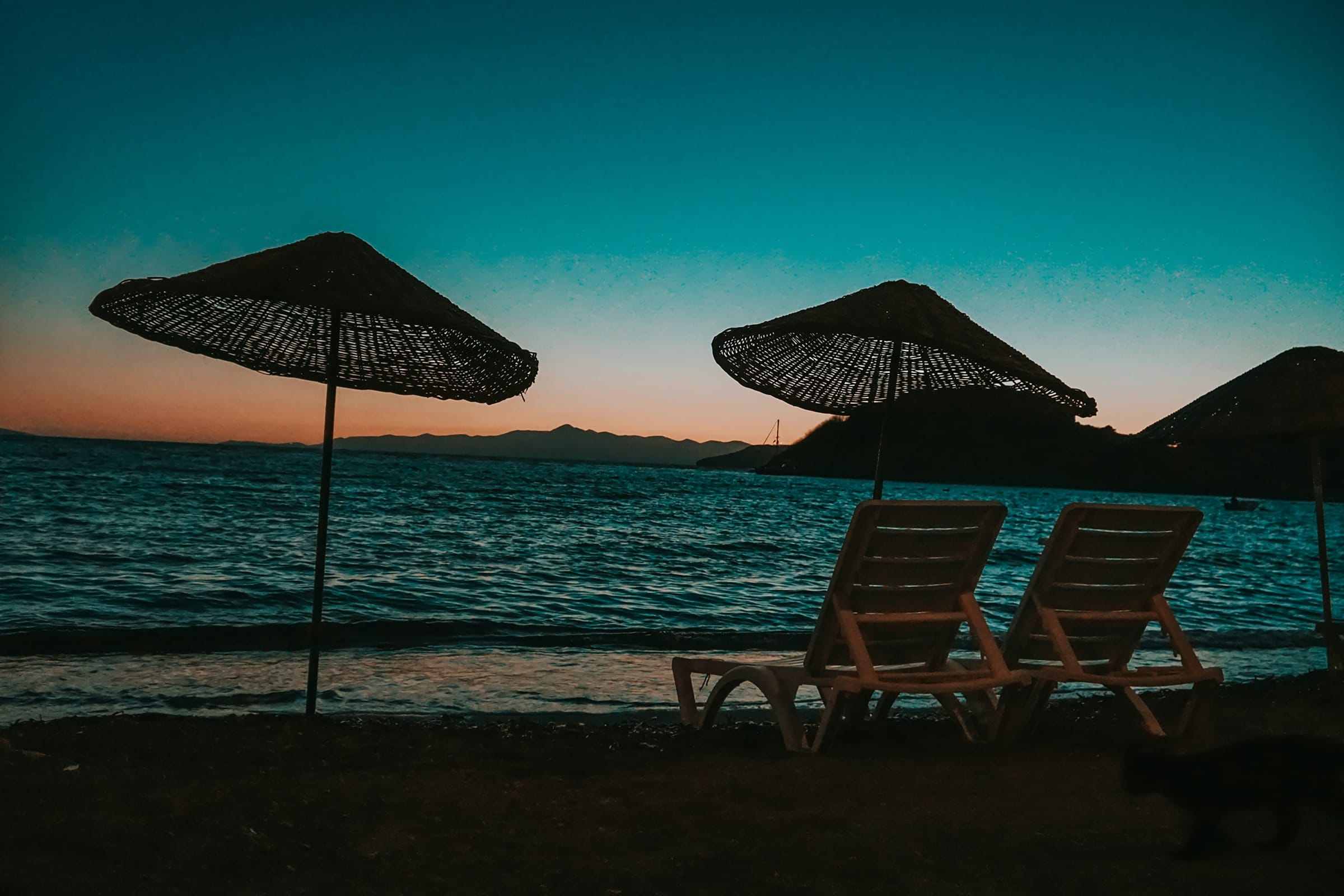 Alacakaranlıkta sahilde hasır şemsiyeler ve şezlonglar